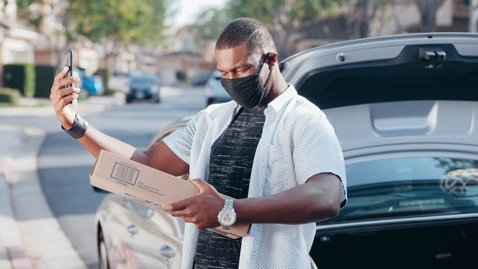 Courier in face mask scanning package in front of car on sunny day, symbolizing efficient service and the value of Bankrate x Coverage - Auto Insurance choices.