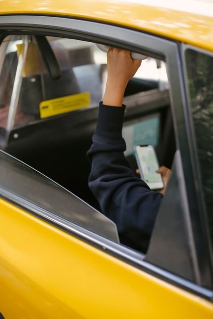 My Insured Ride - Unrecognizable passenger sitting on backseat and browsing smartphone while holding handle inside of yellow cab with lowered window during ride