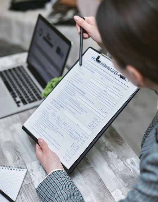 Quote Compare Now Home Insurance (quote compare now home insurance review) Quote Compare Now Home Insurance - An adult reviews a home insurance policy document at a desk with a pen and laptop.